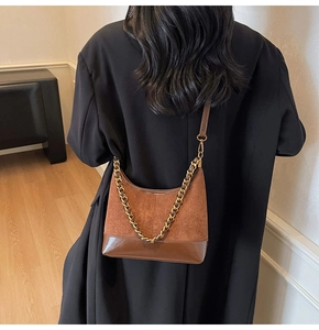 Detail of a brown hobo bag with gold chain strap on a model in a warm indoor setting