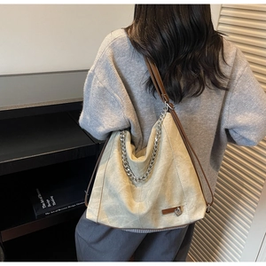 Detail of beige hobo bag with vintage texture, chunky silver chain, and brown leather strap