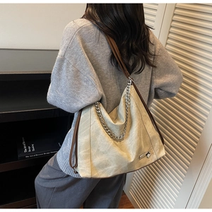 Detail of a large beige tote bag with brown leather straps and silver chain decoration