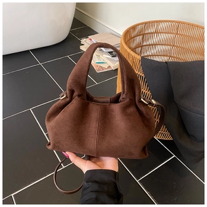 Detail of brown pleated suede bucket bag featuring a smooth metal clasp and slim strap