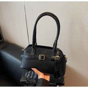 Detail of black faux leather handbag featuring golden metal buckle and decorative strap
