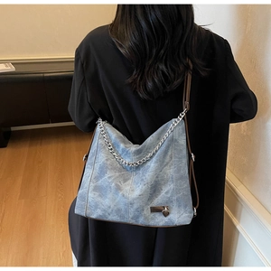 Detail of light blue denim hobo bag with silver chain and heart charm decoration