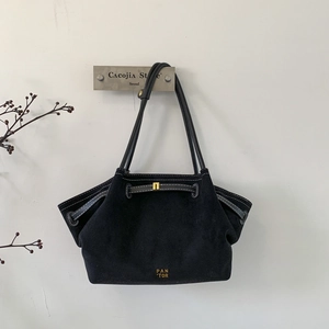 Detail of black suede tote bag with white contrast stitching and gold buckle accents