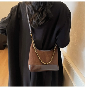 Detail of dark brown leather dumpling bag with chunky gold chain strap on black coat