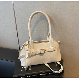 Detail of cream shoulder bag with gold buckle strap on a black book surface