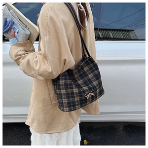 Detail of checkered shoulder bag with golden bow buckle in an outdoor lifestyle setting