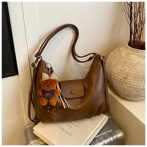 Close-up of a vintage brown leather crescent bag with a cute bear charm on a silver suitcase
