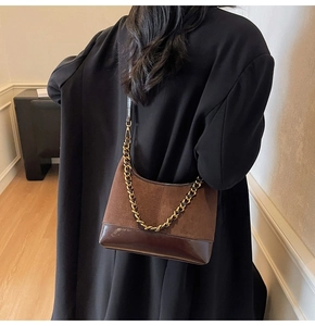 Close-up of brown suede and leather patchwork dumpling bag with gold chain strap detail
