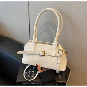Minimalist beige shoulder bag with decorative belt buckle held in a home office setting