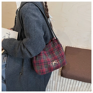 Dettaglio della borsa a quadri rossa e verde con fiocco dorato su un cappotto di lana grigio