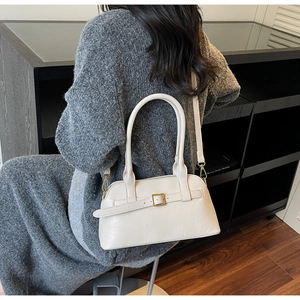 Detail view of cream shoulder bag with gold buckle strap worn by a model in a modern space