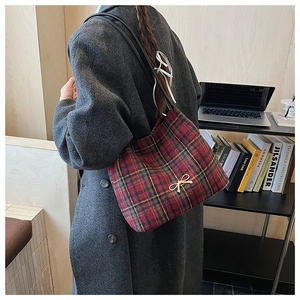 Detail view of plaid bucket bag with gold bow ornament and black leather shoulder strap