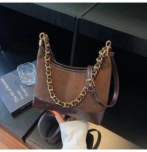 Detail of dark brown dumpling bag with gold chain strap on minimalist black surface