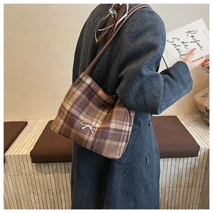 Close-up of brown plaid wool bucket bag with gold bow detail and leather shoulder strap