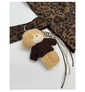 Close-up of a cute plush bear charm in a brown knit sweater on leopard print fabric