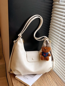 Elegant beige faux leather shoulder bag with cute brown teddy bear charm on wood
