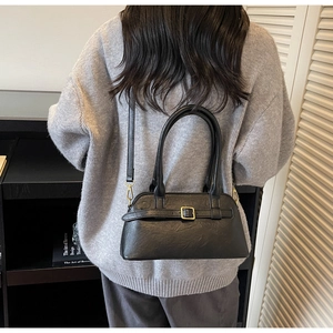 Minimalist black faux leather shoulder bag with gold hardware shown on a model