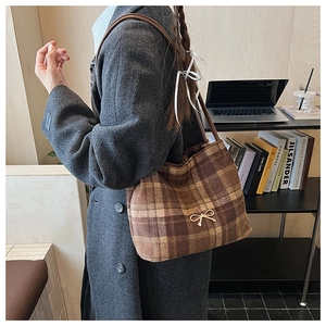 Detail view of brown plaid bucket bag with gold bow buckle and slim leather strap