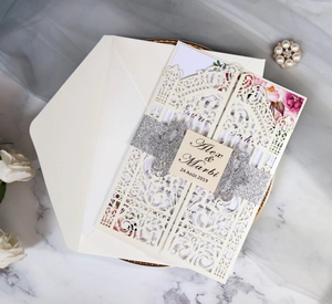 Detail of laser-cut wedding invitation with floral insert and silver glitter belly band