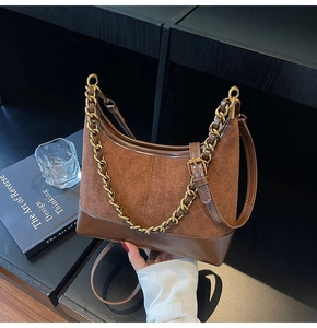 Detail of a brown suede crescent bag with smooth leather trim and chunky gold chain strap