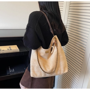 Detail of tan suede tote bag with woven metal chain and wooden bead charm on shoulder