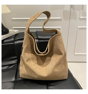 Detail view of khaki suede tote bag with wide strap on a black leather sofa