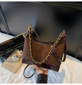 Detail of a brown suede and patent leather shoulder bag with a gold chain strap