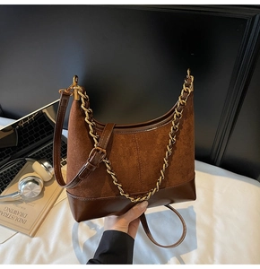 Detail of dark brown hobo bag with suede stitching, gold chain, and adjustable strap