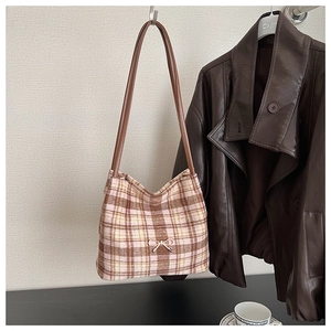 Detail of tweed bucket bag with plaid pattern, golden bow charm and leather strap