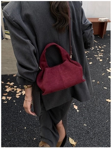 Outdoor street style view of a burgundy suede clutch bag held by a model in a grey suit