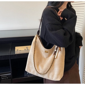 Detail view of beige suede tote bag with chain strap and boho beaded tassel accessory