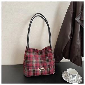 Detail of red plaid bucket bag with gold bow ornament and leather shoulder straps