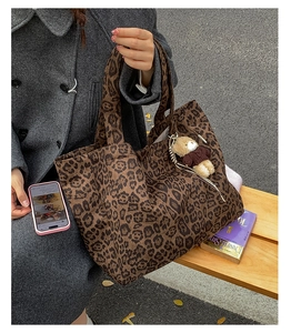 Detail of leopard print canvas tote bag with a cute plush bear charm in a street setting