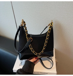 Detail of black saddle bag featuring matte suede and smooth leather with gold chain link