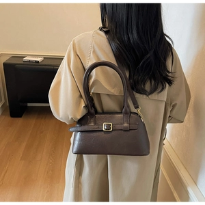 Detail of a vintage dark brown leather shoulder bag with a gold buckle shown on a model
