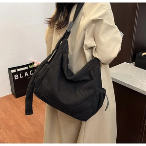 Side view of the large black corduroy crossbody tote bag worn with a beige trench coat
