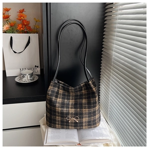 Close-up of tartan pattern bucket bag with golden bow accent on casual lifestyle background