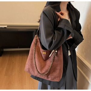 Detail view of brown suede tote bag with metal chain strap and wooden bead charm