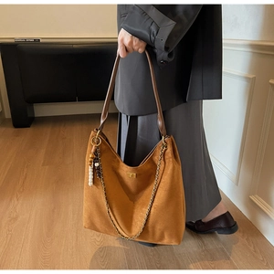 Detail of caramel suede tote bag with golden chain and wooden bead charm on shoulder