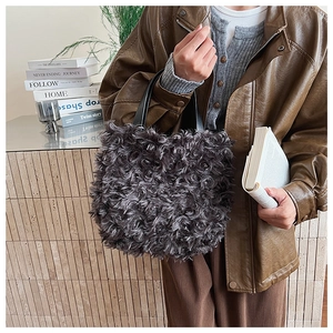 Dettaglio della borsa a secchiello in peluche grigio scuro con trama riccia e manici in pelle