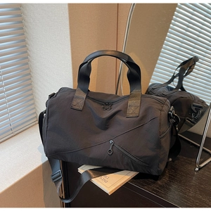 Détail de la poche zippée diagonale et de l'anneau sur le sac fourre-tout en nylon noir