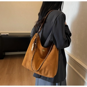 Brown suede tote bag with metal chain and wooden bead charm shown on shoulder