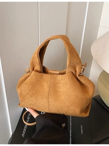 Retro tan faux suede handbag with wide handle and crossbody strap on book background