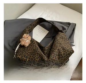 Detail of leopard print hobo bag with a plush bear charm on white fabric and blazer
