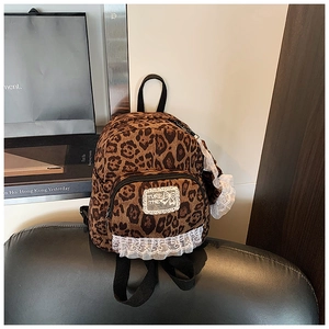 Detail view of mini leopard print backpack with white lace trim on a black leather stool