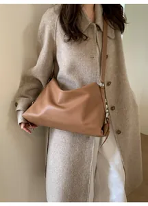 Brown leather tote bag worn over a beige coat showing side strap and buckle detail