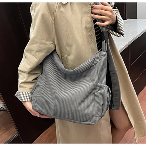 Detail of grey corduroy crossbody tote bag with side drawstring pocket worn with a coat