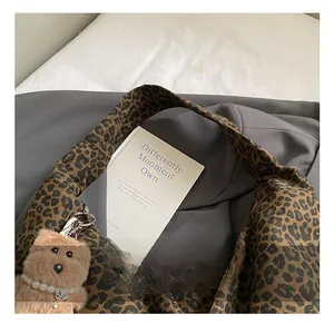 Detail of leopard print tote bag featuring a plush bear charm and textured handle