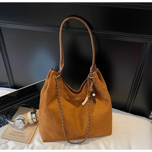 Brown suede hobo bag with gold hardware and boho beads placed next to laptop and headphones