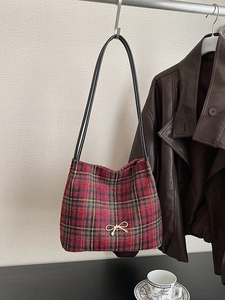 Classic red plaid bucket bag with gold bow clasp, hanging in an autumn setting